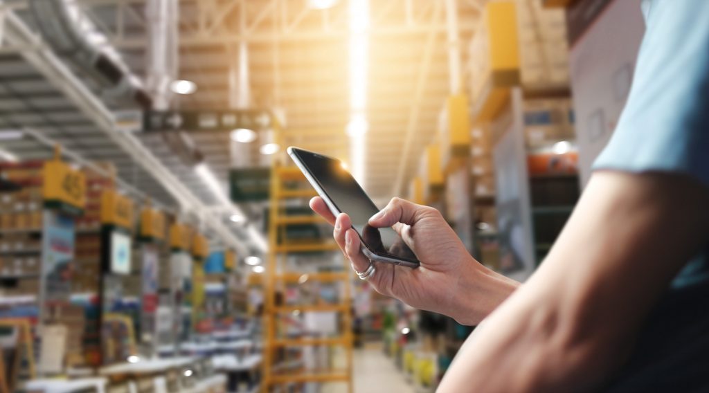 Factory worker using application on mobile smartphone to operrate automation for modern trade. Checking order in large warehouse. Import and export the shipping cargo. (Bild: ©ipopba/stock.adobe.com)